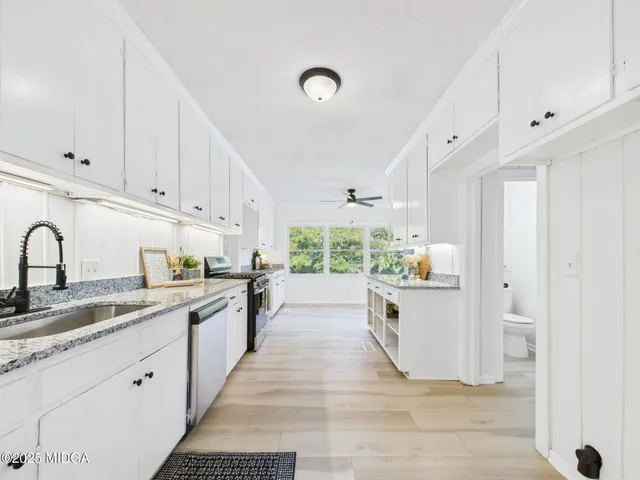 a large kitchen with stainless steel appliances kitchen island granite countertop a stove a sink a refrigerator white cabinets and wooden floor next to a window
