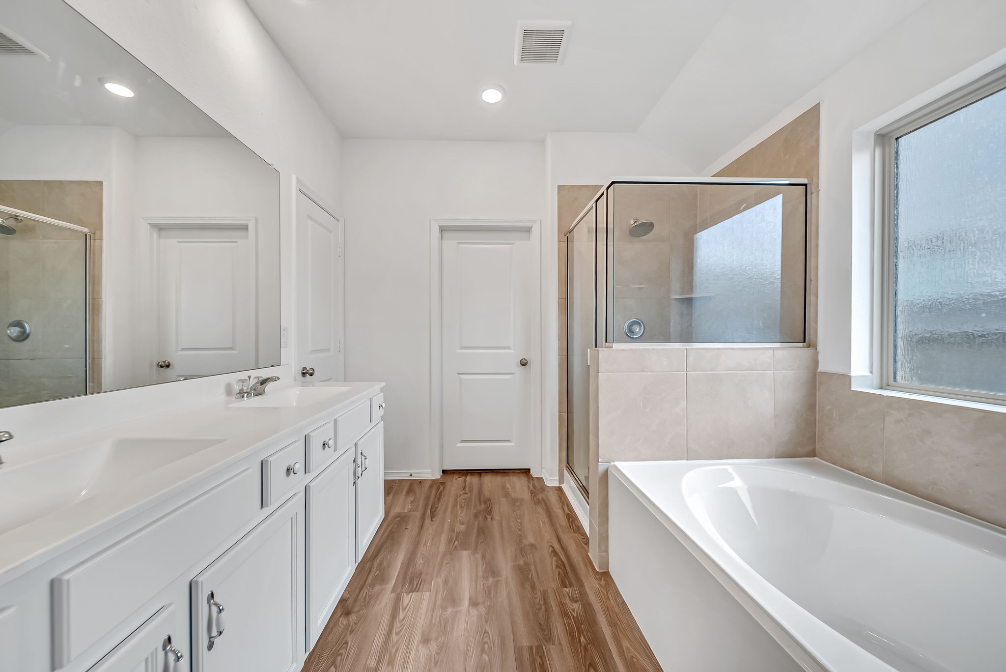 2847 Mistygate Court Conroe, TX 77301 - Photo 16 of 27 Bright and spacious bathroom featuring a large vanity with dual sinks, a glass-enclosed shower, and a separate soaking tub. The room has stylish wood flooring and ample natural light from a frosted window.