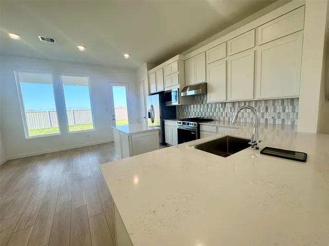a kitchen with stainless steel appliances kitchen island granite countertop a refrigerator a sink dishwasher and white cabinets with wooden floor