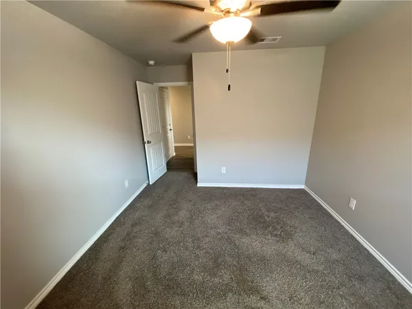 an empty room with a chandelier fan and wooden floor