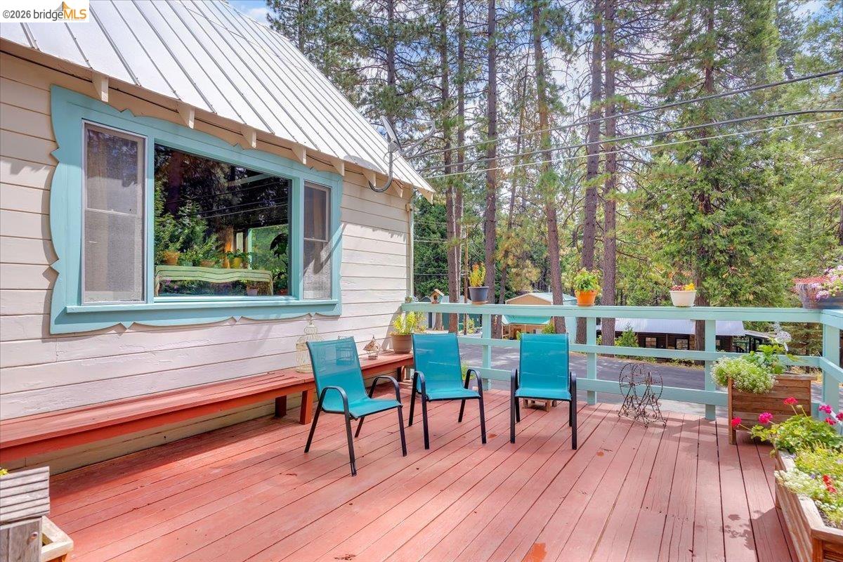 26144 Long Barn Road Long Barn, CA 95335 - Photo 35 of 42 Expansive red-stained deck with a built-in bench, light blue railing, and decorative window trim, all surrounded by mature trees