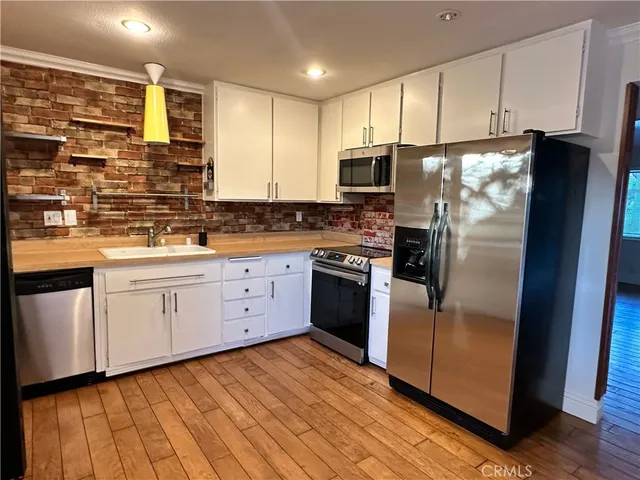 a kitchen with stainless steel appliances granite countertop a refrigerator a sink dishwasher a stove with wooden cabinets and floors