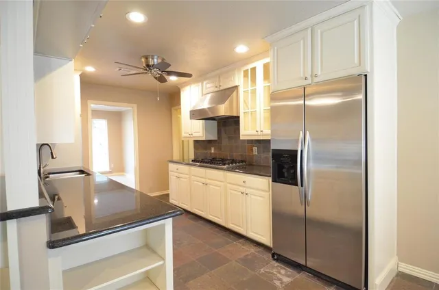a kitchen with stainless steel appliances granite countertop a refrigerator a sink and white cabinets