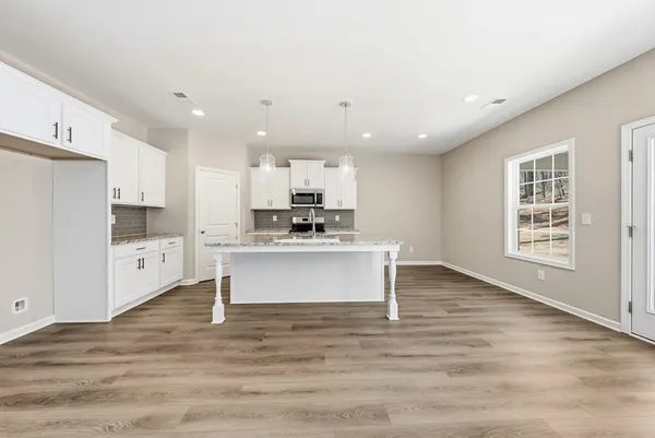 a view of kitchen with granite countertop refrigerator and white cabinets with wooden floor