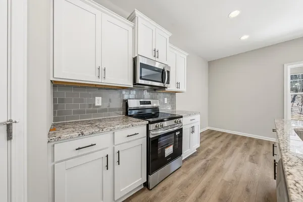 a kitchen with stainless steel appliances granite countertop a stove a microwave and white cabinets