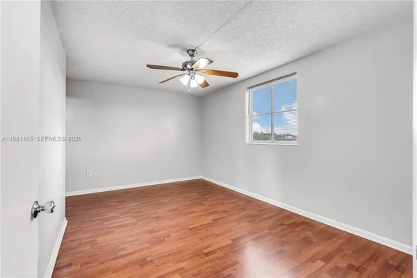 an empty room with wooden floor ceiling fan and window