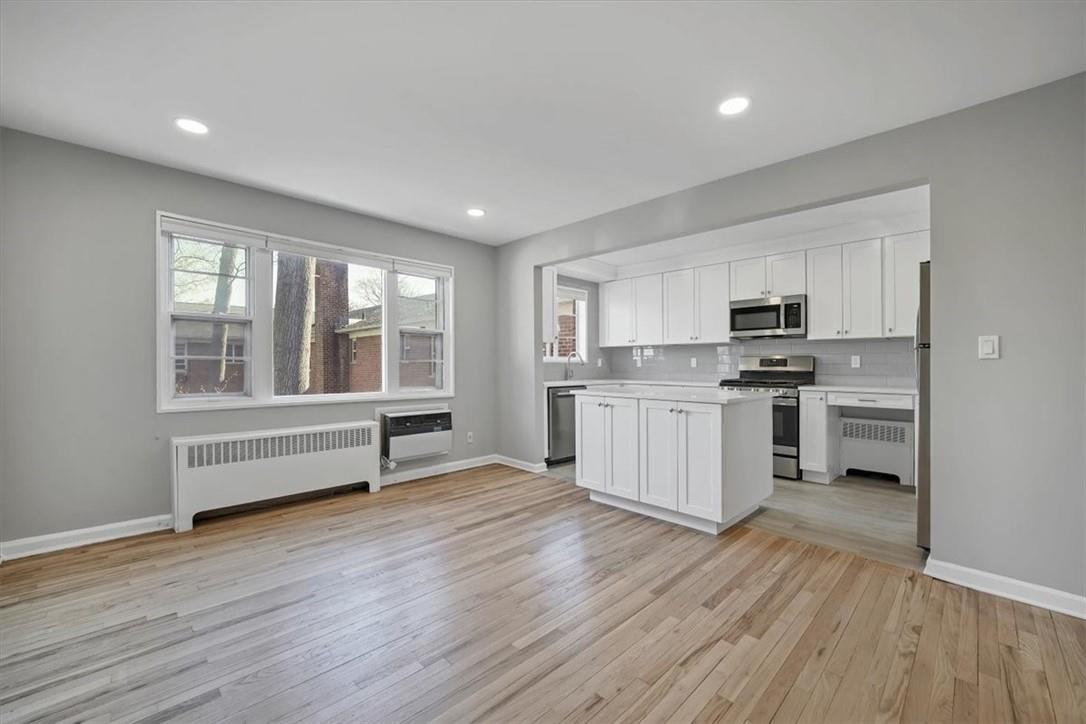 Kitchen featuring stainless steel appliances, white cabinetry, light hardwood / wood-style flooring, and radiator heating unit