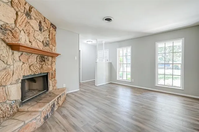 an empty room with wooden floor fireplace and windows