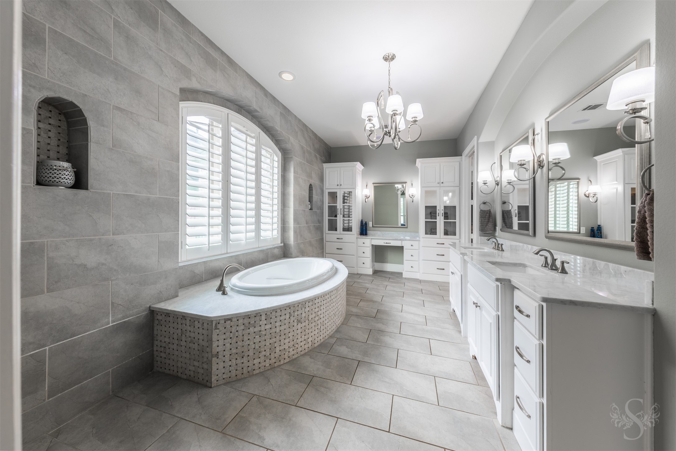 28602 Hoffman Spring Lane Fulshear, TX 77441 - Photo 21 of 49 Spa-inspired primary bath showcases a soaking tub set beneath a large window with plantation shutters, framed by extensive tilework and architectural detailing. The expansive layout includes a dedicated vanity area with abundant cabinetry and storage.