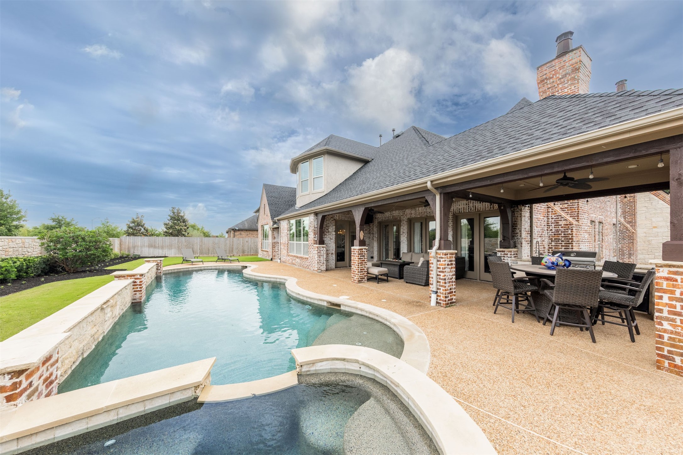 28602 Hoffman Spring Lane Fulshear, TX 77441 - Photo 40 of 49 Stunning backyard retreat centers around a custom-designed pool and spa with elegant water features, expansive decking, and beautifully integrated hardscaping. The covered patio with outdoor kitchen and multiple seating areas creates a seamless indoor-outdoor experience, offering an exceptional setting for both everyday enjoyment and large-scale entertaining.