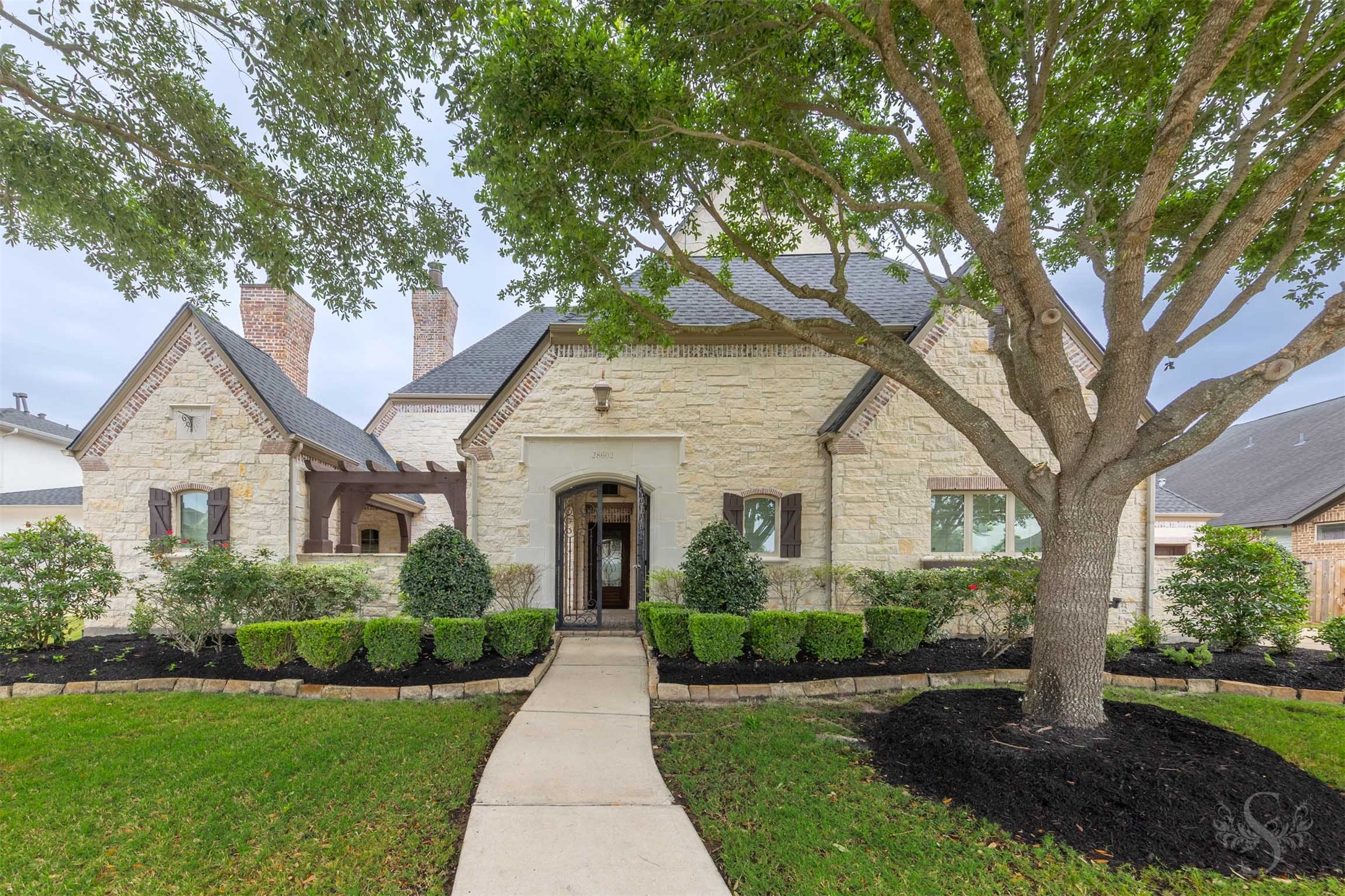 28602 Hoffman Spring Lane Fulshear, TX 77441 - Photo 48 of 49 Exceptional Huntington Homes design showcases timeless stone architecture, rich exterior detailing and a welcoming gated front entry that sets the tone for the luxury found throughout. Mature trees and beautifully manicured landscaping enhance the home’s impressive curb appeal in the gated Legacy at Cross Creek Ranch community.