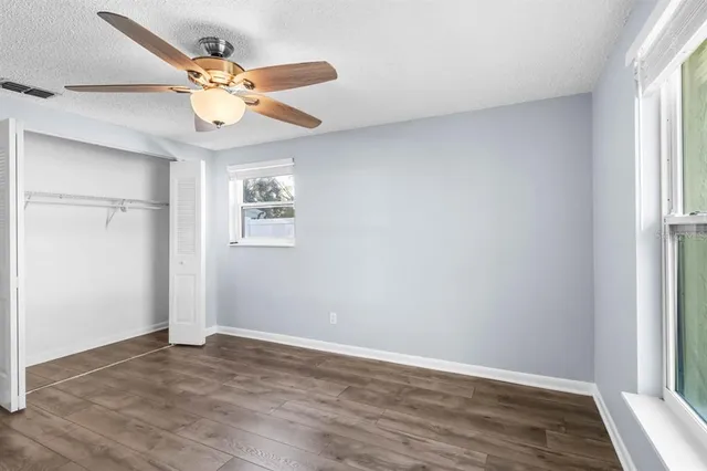 an empty room with wooden floor fan and windows