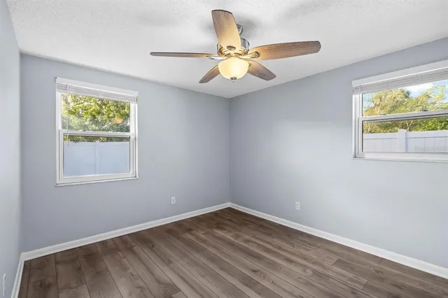 an empty room with wooden floor fan and windows
