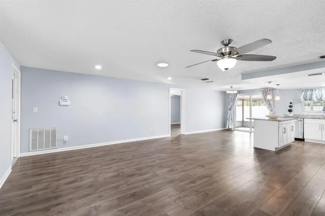 a view of an empty room and kitchen view with wooden floor