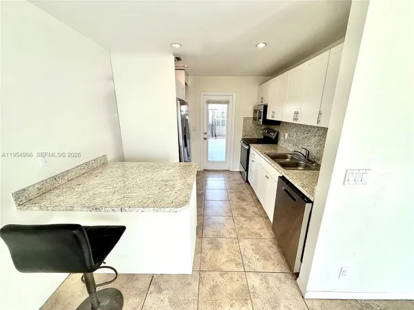 a large kitchen with granite countertop a sink and white cabinets