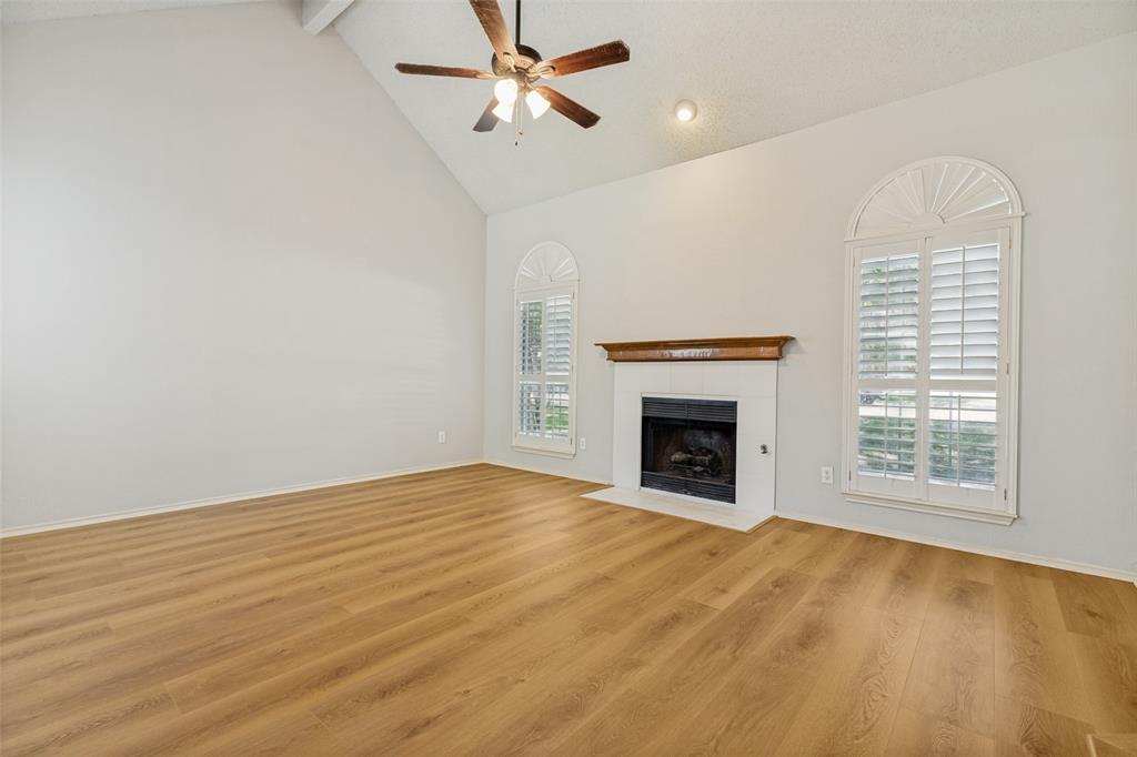 1215 Spring Creek Drive Allen, TX 75002 - Photo 5 of 40 Living area featuring vaulted ceilings, wood-finish flooring, a fireplace with a white surround and wood mantel, and arched windows with plantation shutters