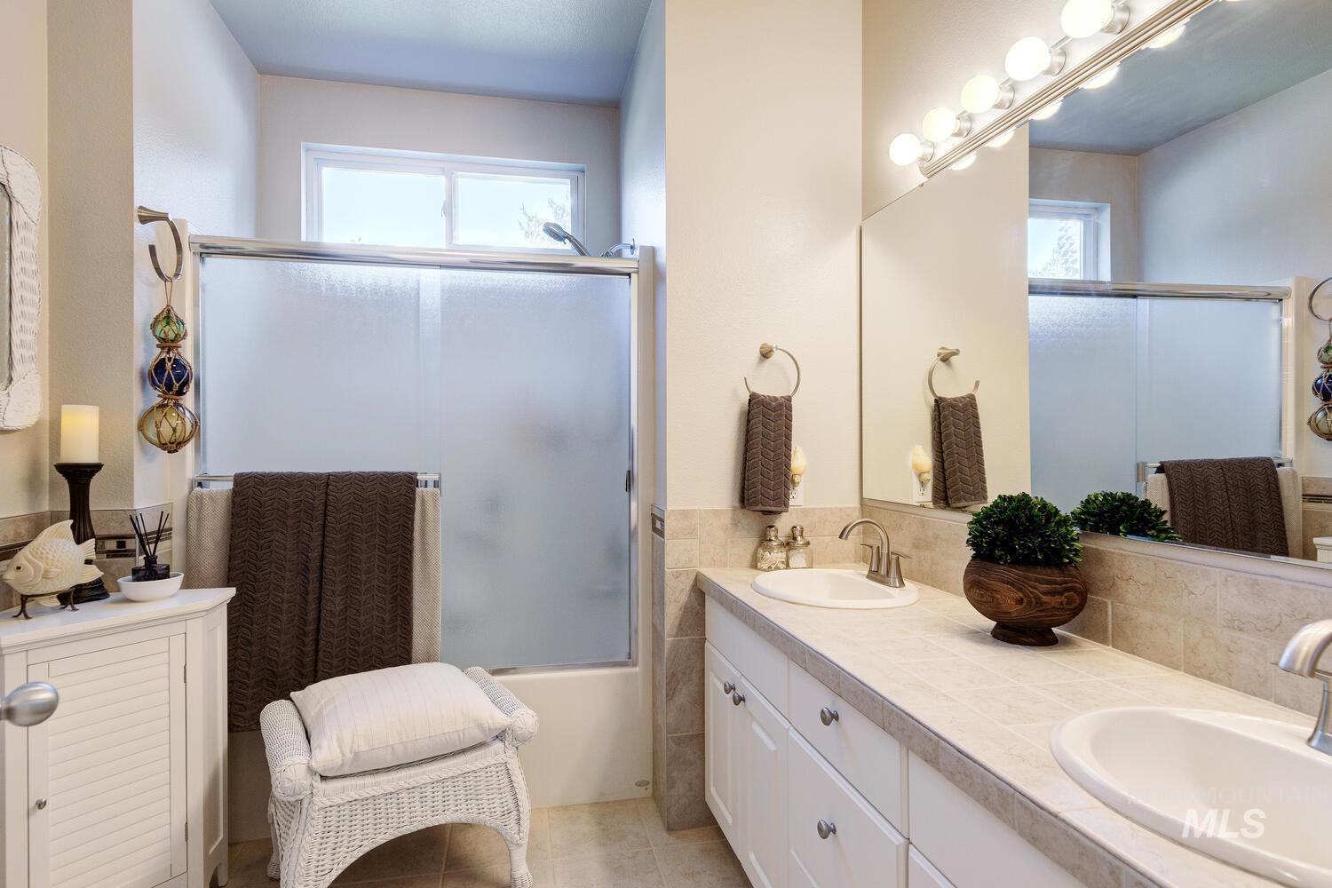 10585 West Vega Court Star, ID 83669 - Photo 24 of 49 Bathroom featuring double vanity, plenty of natural light, bath / shower combo with glass door, and light tile patterned floors