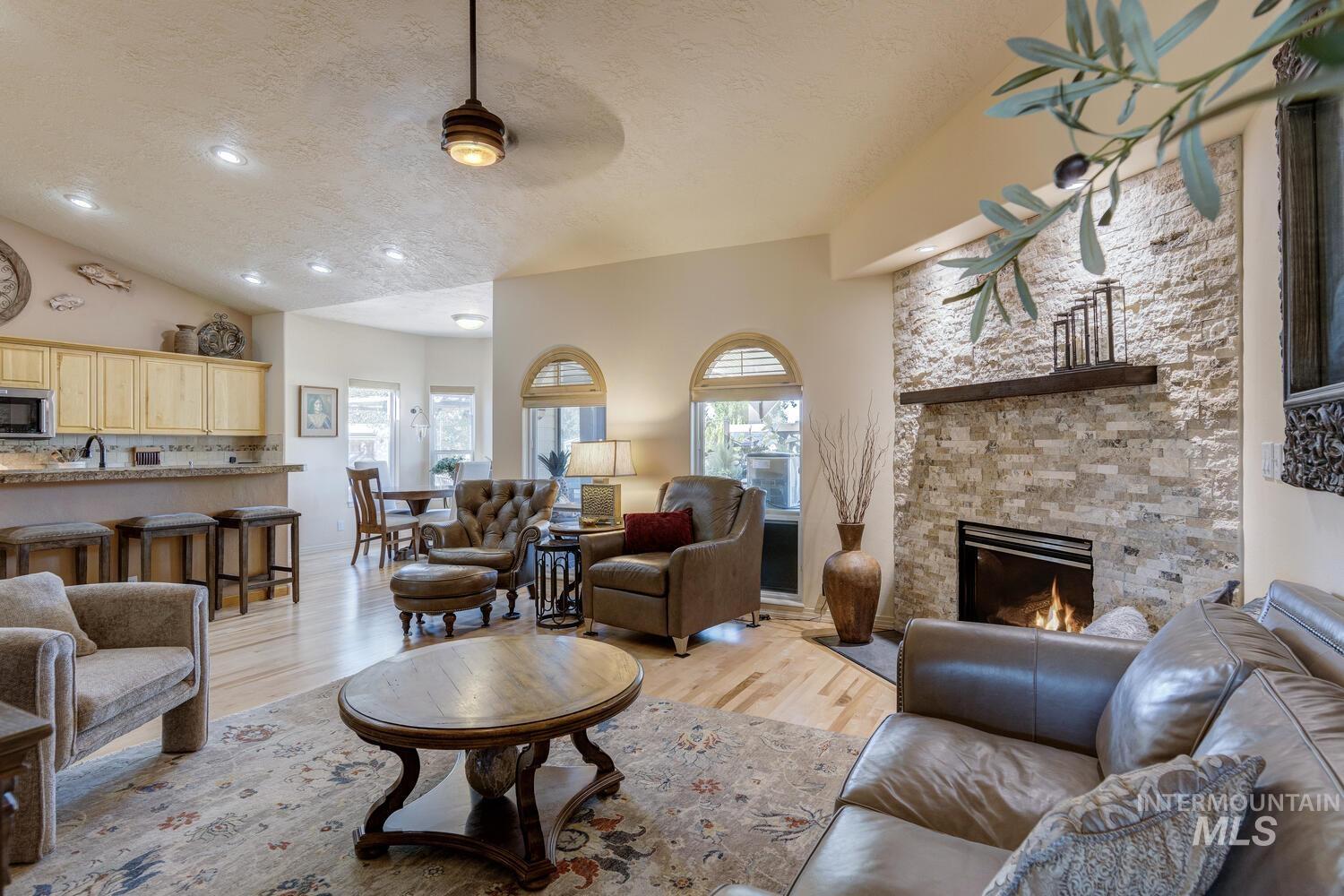 10585 West Vega Court Star, ID 83669 - Photo 5 of 49 Living area with a textured ceiling, a stone fireplace, light wood finished floors, a ceiling fan, and vaulted ceiling