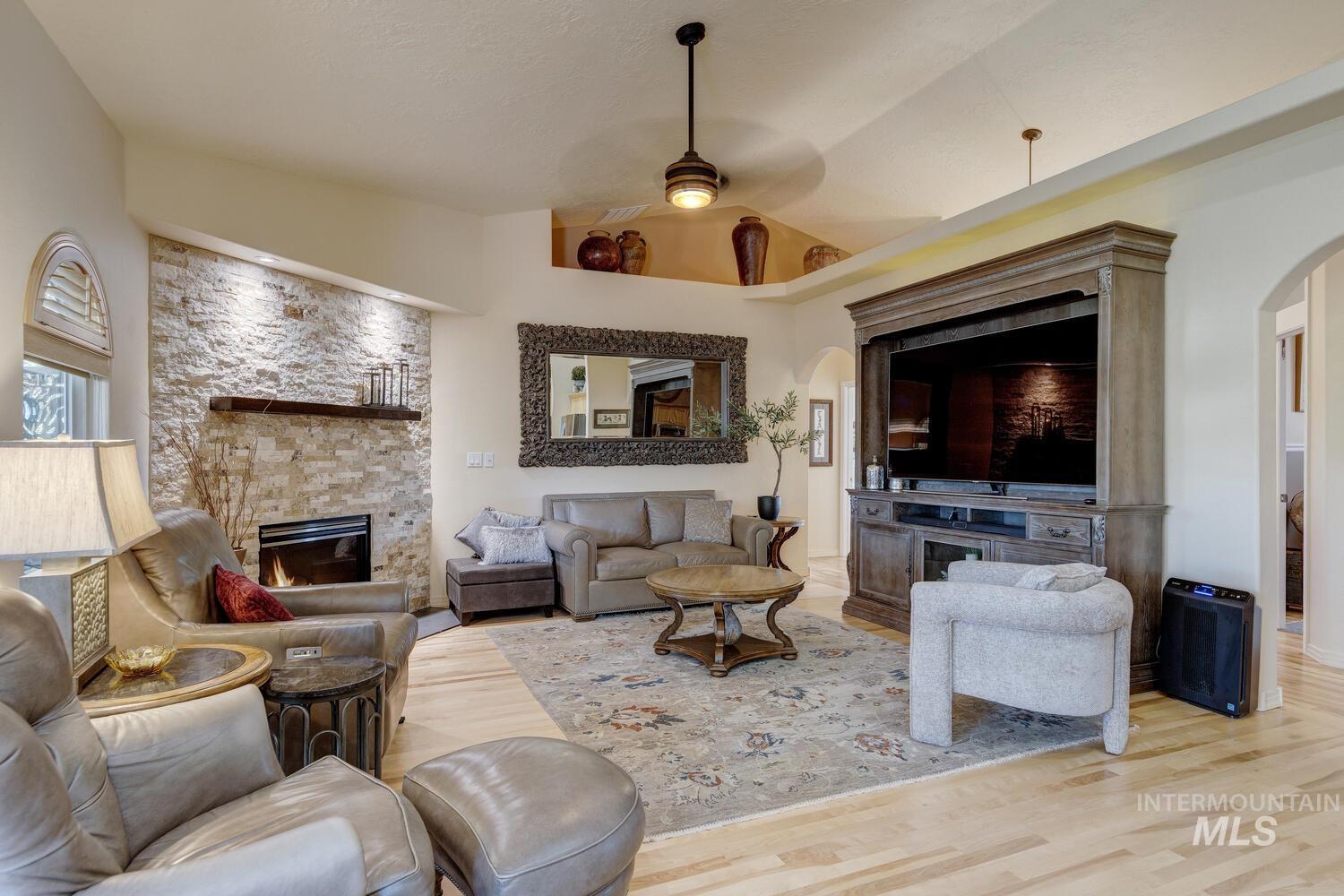 10585 West Vega Court Star, ID 83669 - Photo 9 of 49 Living area featuring arched walkways, a stone fireplace, wood finished floors, ceiling fan, and lofted ceiling