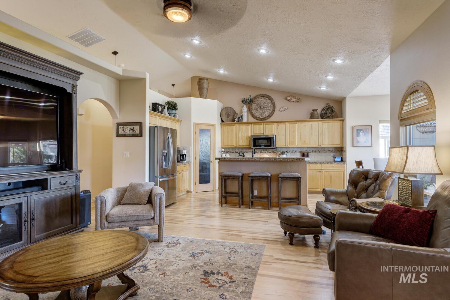 10585 West Vega Court Star, ID 83669 - Photo 10 of 49 Living room featuring a textured ceiling, light wood-style floors, arched walkways, recessed lighting, and high vaulted ceiling