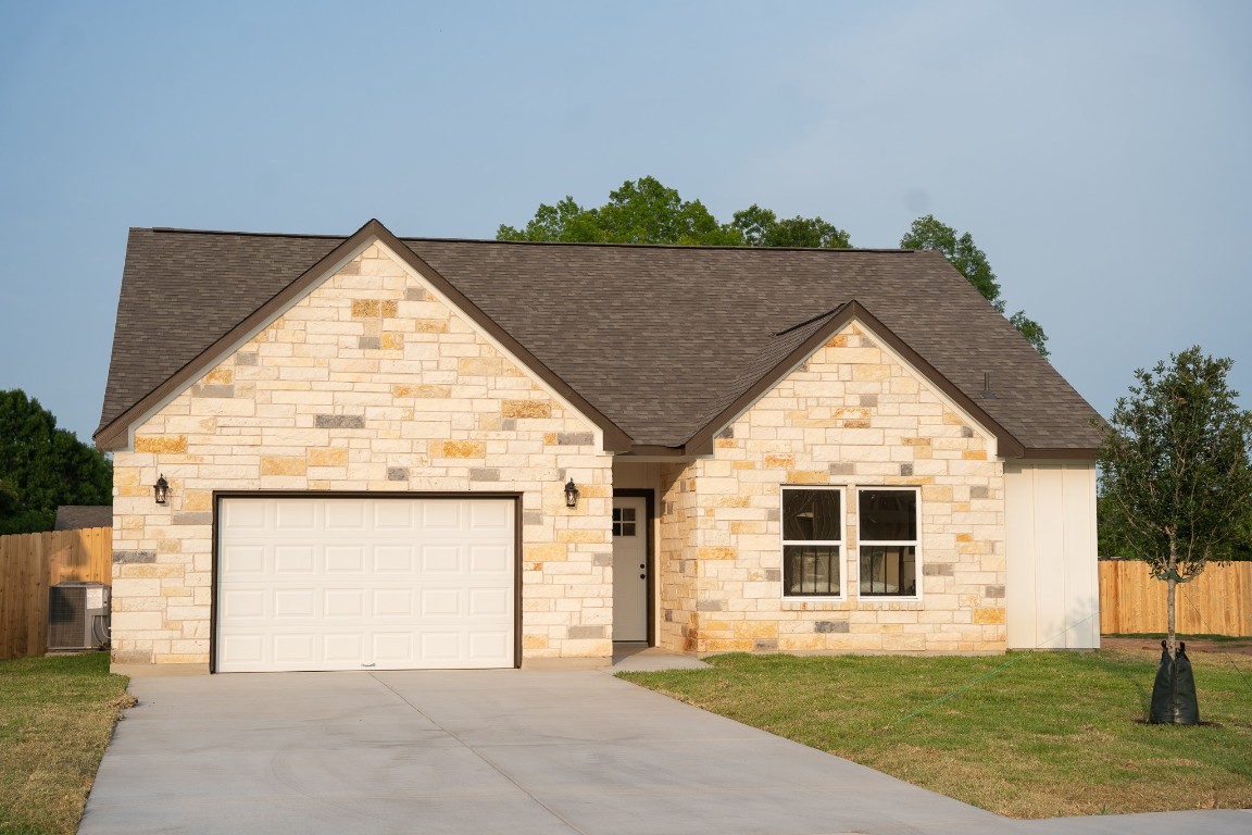 304 String Prairie Way Smithville, TX 78957 - Photo 6 of 30 French country style house with a shingled roof, concrete driveway, an attached garage, cooling unit, and stone siding