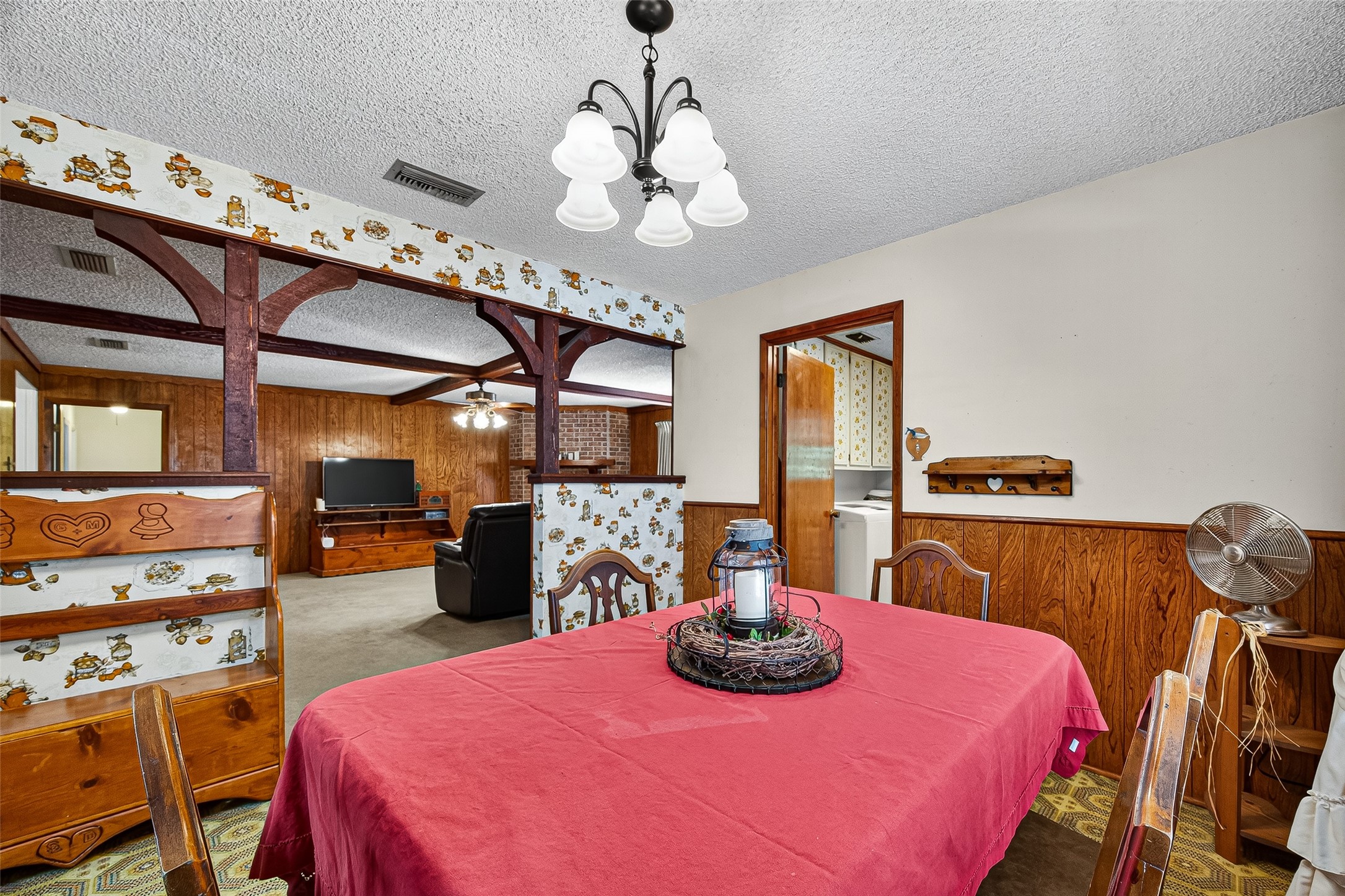 12021 7th 1/2 Street Santa Fe, TX 77510 - Photo 20 of 49 Cozy dining area with vintage charm, featuring wood paneling, patterned wallpaper, and decorative beams. The space is open to a living room with a TV, offering a warm and inviting atmosphere.