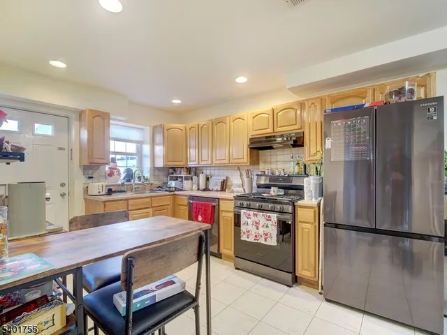 a kitchen with stainless steel appliances granite countertop a refrigerator a stove a sink a dining table and chairs with wooden floor