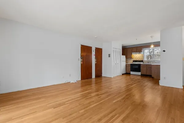 an empty room with wooden floor and kitchen view