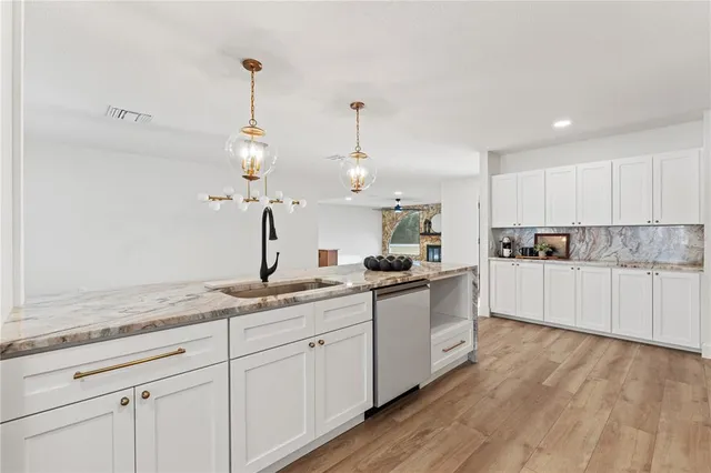 a kitchen with stainless steel appliances kitchen island granite countertop a refrigerator a stove a sink dishwasher and white cabinets with wooden floor