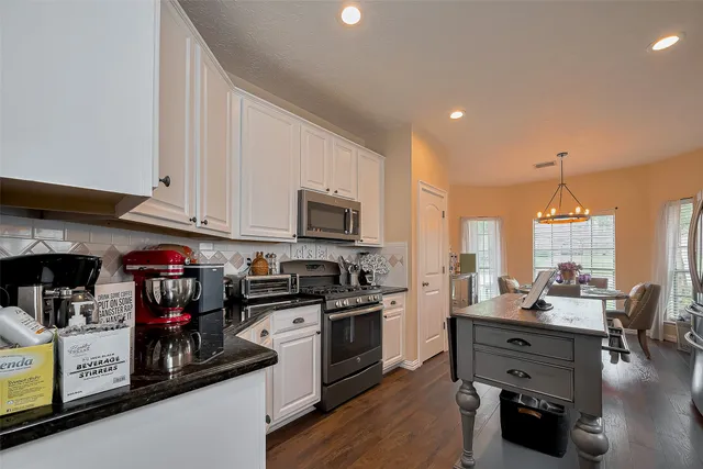 a kitchen with stainless steel appliances kitchen island granite countertop a stove top oven a sink dishwasher and white cabinets with wooden floor