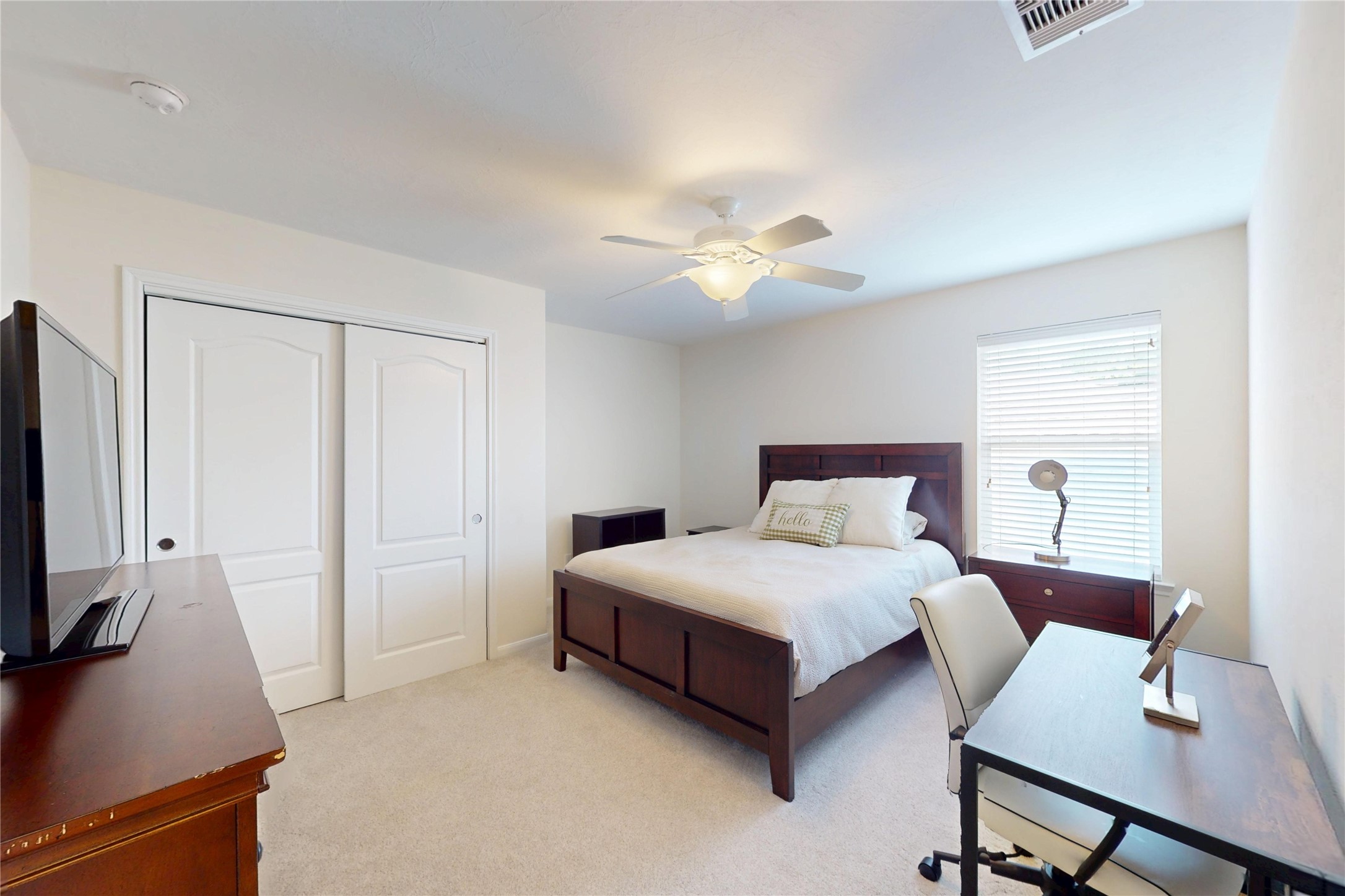 17402 Rainer Valley Lane Humble, TX 77346 - Photo 25 of 33 This is a bright, cozy bedroom featuring a double bed, a ceiling fan, and a window with blinds. It includes a desk and chair, a TV on a dresser, and a closet with sliding doors. The neutral walls and carpet create a warm atmosphere.
