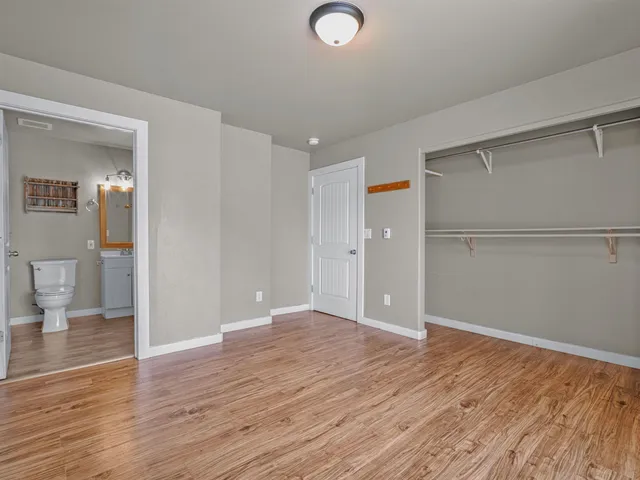 a view of an empty room with wooden floor and a bathroom