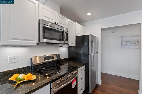 a kitchen with granite countertop white cabinets a sink a stove and wooden floors