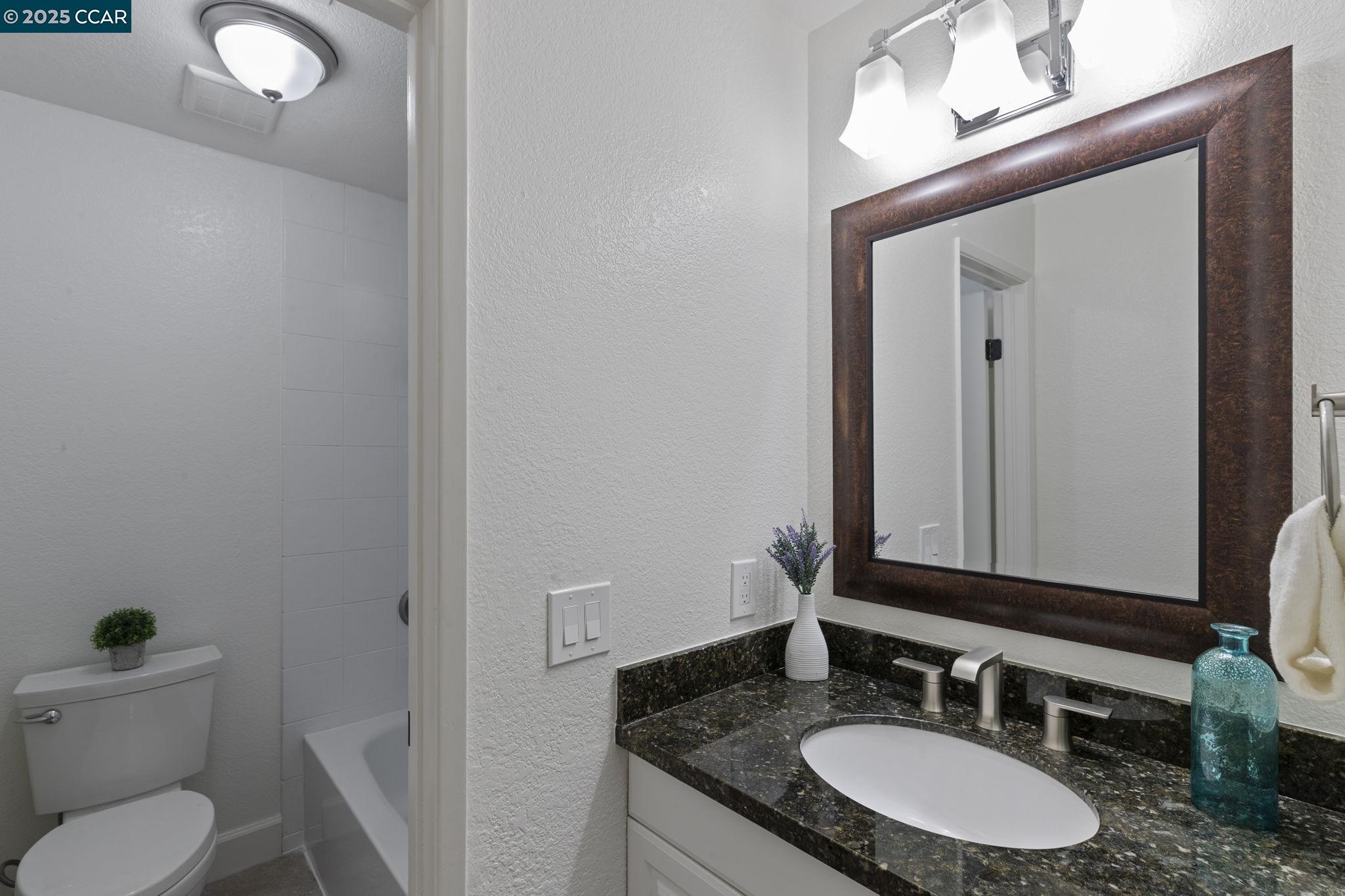 5050 Valley Crest Drive, Unit 63 Concord, CA 94521 - Photo 35 of 55 a bathroom with a granite countertop sink toilet a mirror and bathtub