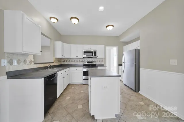 a kitchen that has a lot of white cabinets and stainless steel appliances