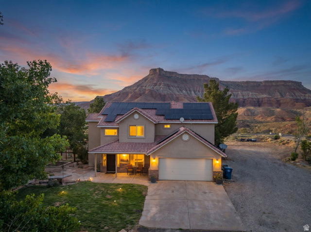 1440 West 100 South Virgin, UT 84779 - Photo 2 of 45 Stucco exterior residence with solar panels and an attached garage, featuring a tile roof and a covered front porch, all set against a prominent mountain backdrop