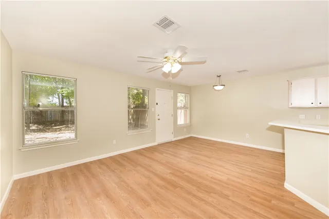 an empty room with wooden floor fan and windows