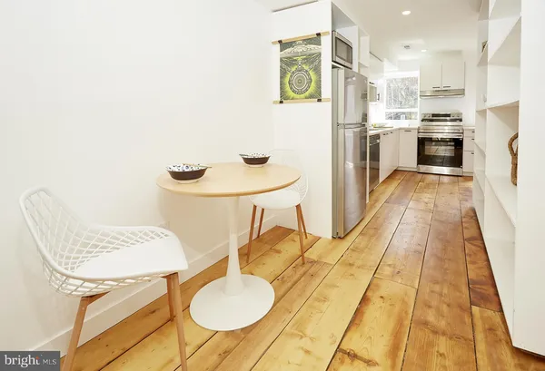 a kitchen with stainless steel appliances granite countertop a sink a stove a refrigerator a dining table and chairs with wooden floor