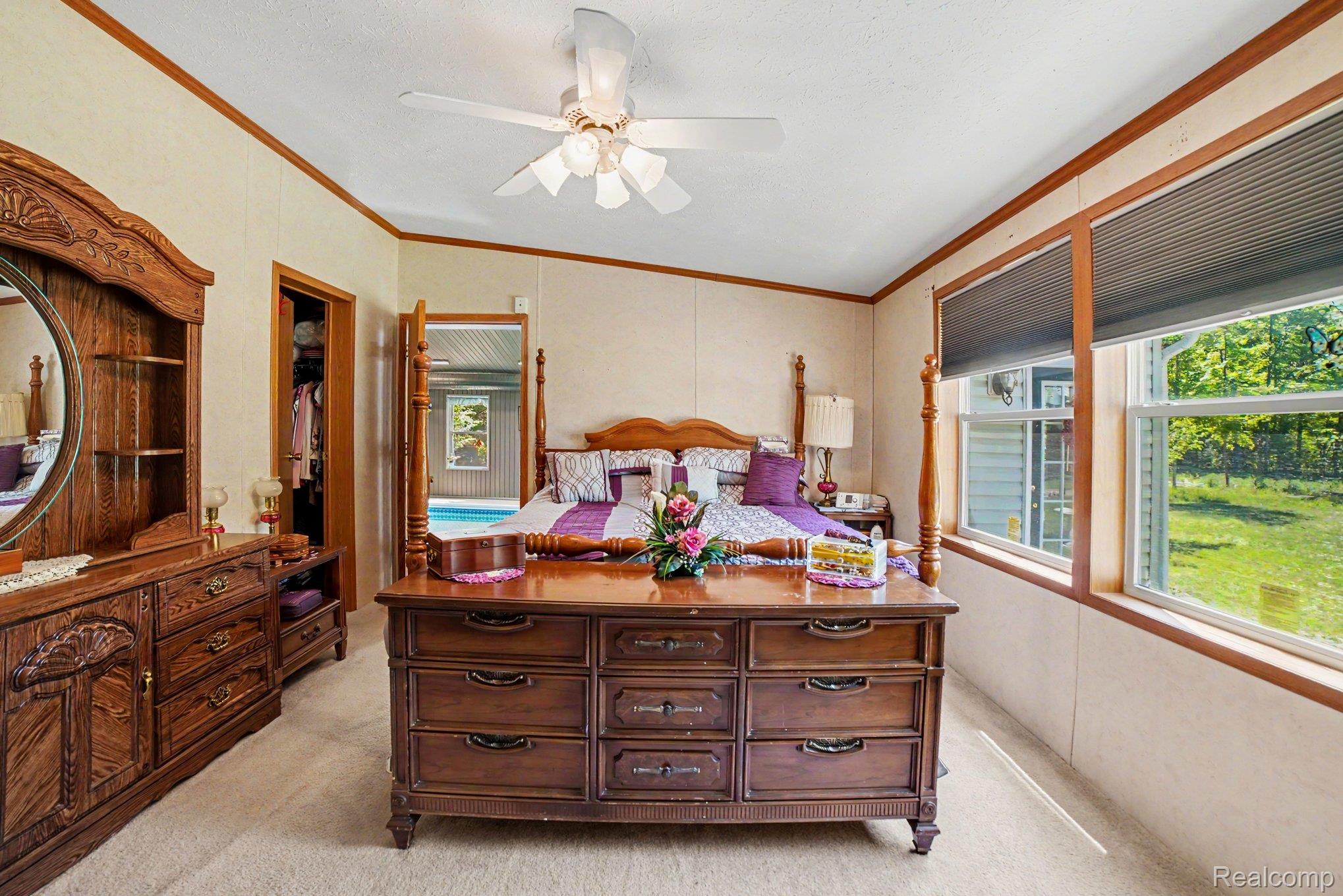 4772 South Bard Road Beaverton, MI 48612 - Photo 25 of 46 Carpeted room featuring a ceiling fan, wood trim, multiple windows with blinds, and a door opening to a visible pool area