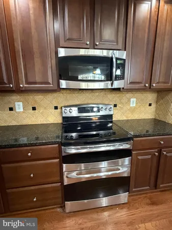 a stove top oven sitting inside of a kitchen with granite countertop wooden cabinets