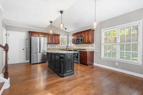 a kitchen with stainless steel appliances granite countertop a stove a sink a refrigerator and a wooden floor
