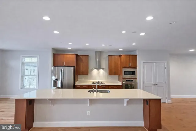 a view of a kitchen with kitchen island a sink wooden floor and stainless steel appliances