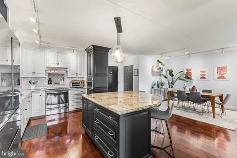 a kitchen with stainless steel appliances kitchen island granite countertop a stove refrigerator and dining table with wooden floor