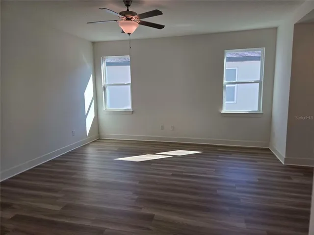a view of empty room with wooden floor and fan