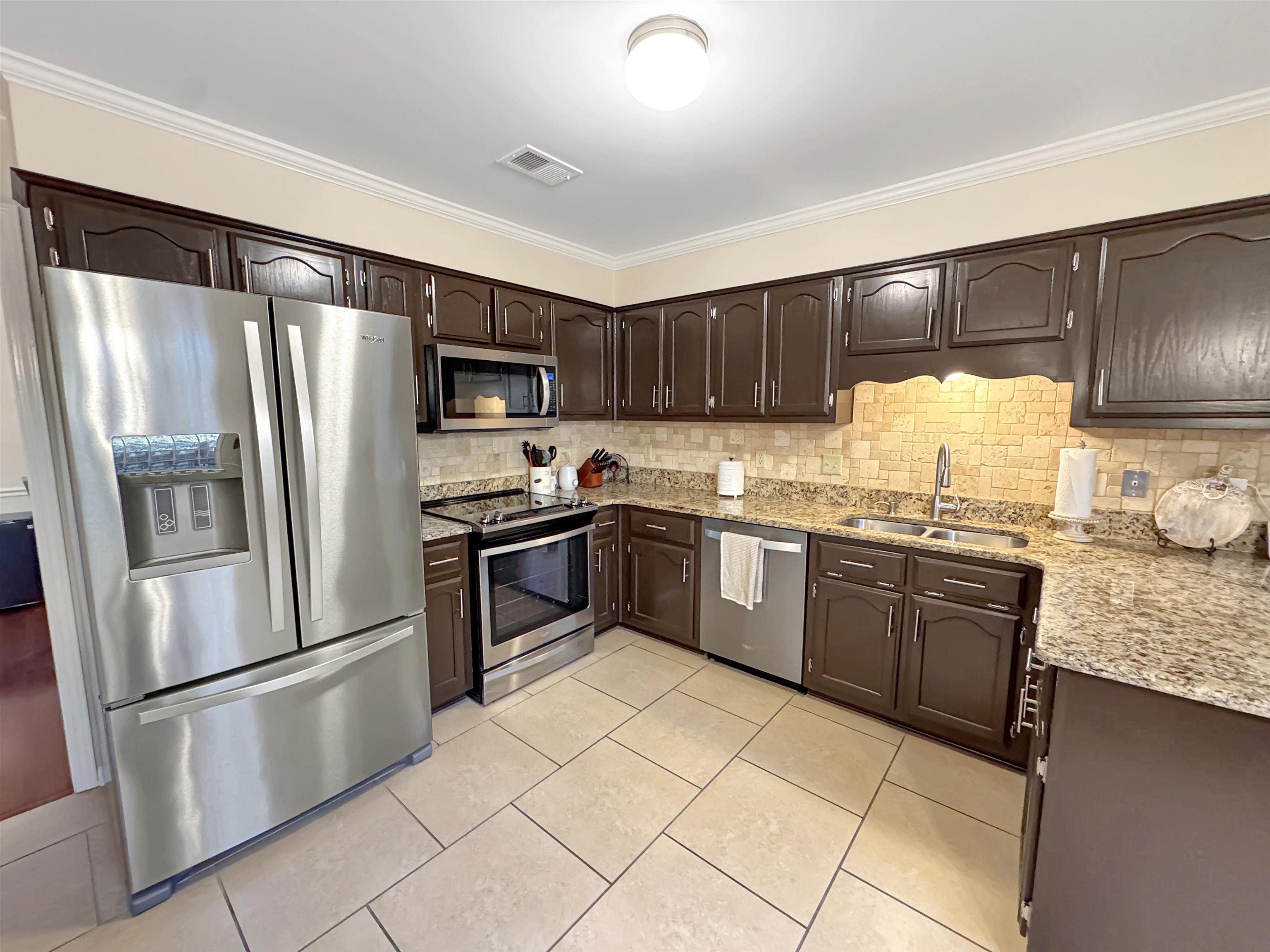 340 Scarlett's Way Collierville, TN 38017 - Photo 14 of 40 Kitchen featuring appliances with stainless steel finishes, dark brown cabinetry, ornamental molding, light stone counters, and tasteful backsplash