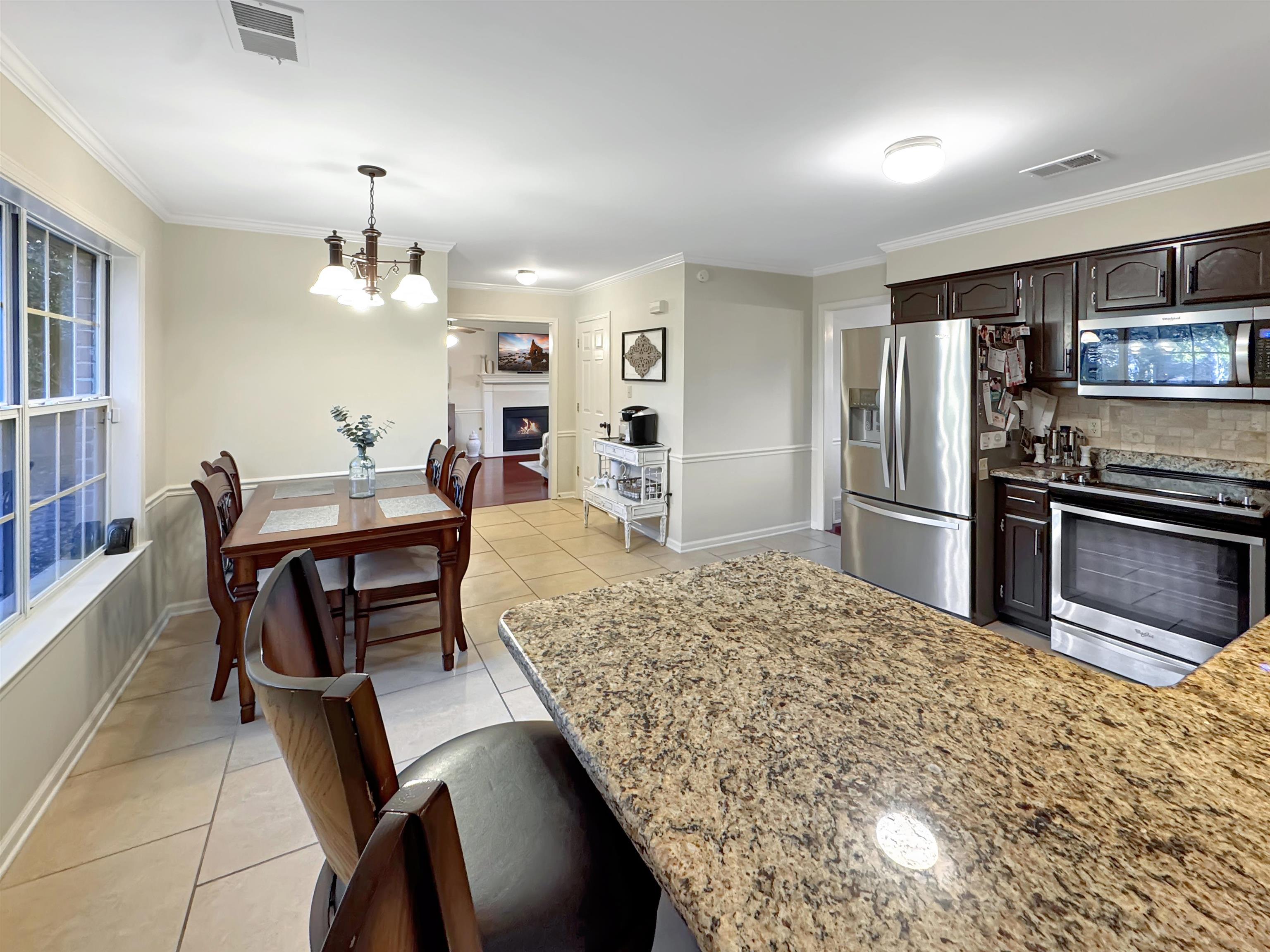 340 Scarlett's Way Collierville, TN 38017 - Photo 10 of 40 Kitchen featuring appliances with stainless steel finishes, light tile patterned floors, ornamental molding, a lit fireplace, and light stone counters