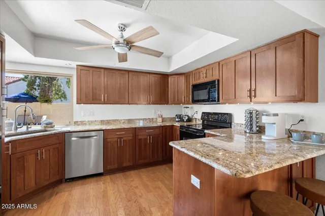 a kitchen with stainless steel appliances granite countertop wooden cabinets a sink dishwasher a stove and a refrigerator with wooden floor