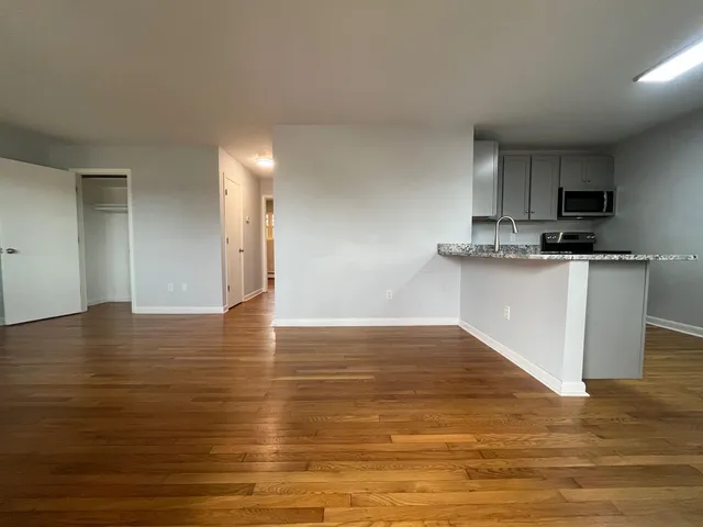 a view of kitchen and empty room with wooden floor