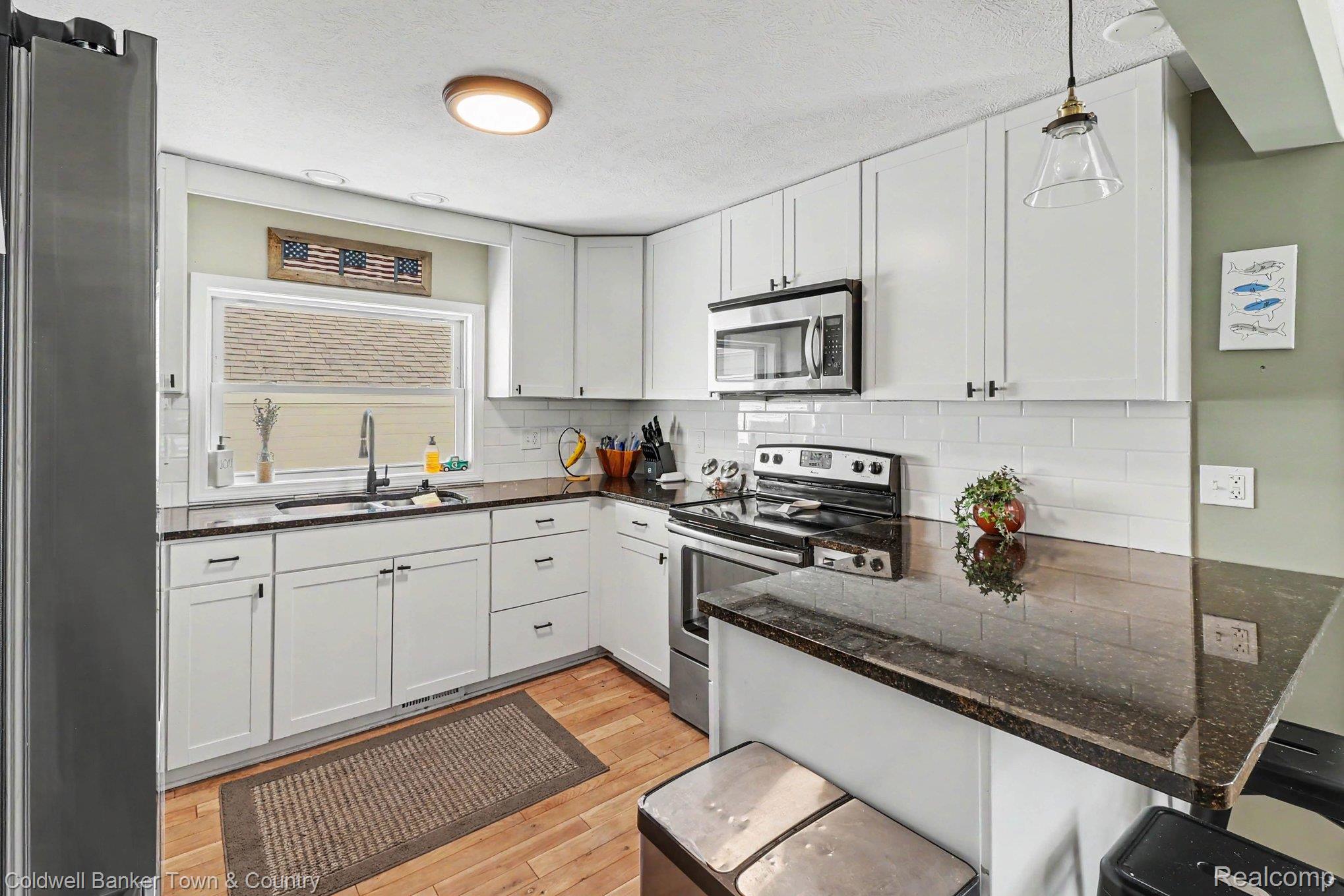 4240 Moyer Road Williamston, MI 48895 - Photo 8 of 21 Updated kitchen featuring white shaker cabinetry, dark countertops, a white subway tile backsplash, stainless steel appliances, and wood-finish flooring