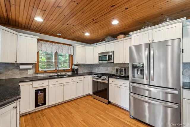 a large kitchen with stainless steel appliances granite countertop a stove a sink and white cabinets with wooden floor